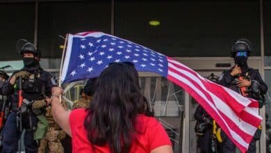 Photo: A woman agitates an American flag, while the staff of the California National Guard is outside the Federal Building during protests in response to federal immigration operations in Los Angeles, on June 10, 2025.