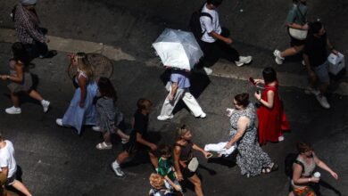 Photo: pedestrians, including a person holding an umbrella to block UV rays, walk on Times Square in New York