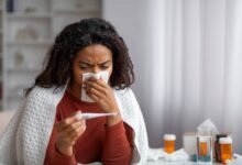 PHOTO: Sick black woman blowing her runny nose and looking at thermometer at home