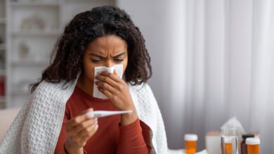 PHOTO: Sick black woman blowing her runny nose and looking at thermometer at home