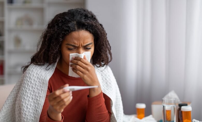 PHOTO: Sick black woman blowing her runny nose and looking at thermometer at home